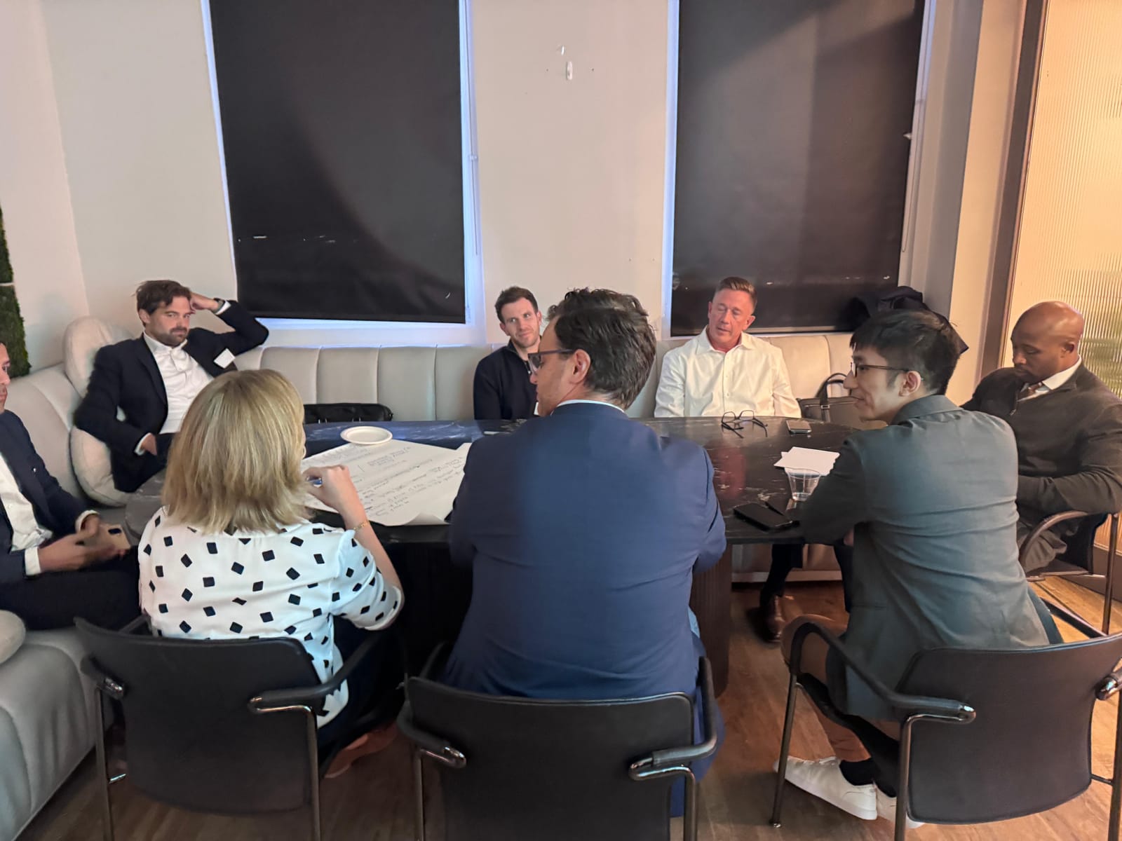 Roundtable participants seated around a table during a facilitated discussion, with notes being taken on a large sheet of paper