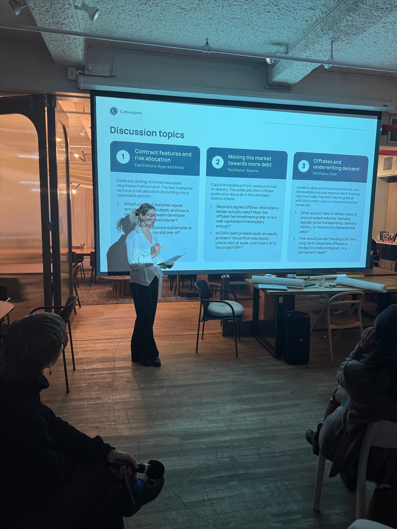 A presenter introducing the roundtable’s three discussion topics in front of a Carbonaires slide listing contract features and risk allocation, moving the market towards more debt, and offtakes and underwriting demand