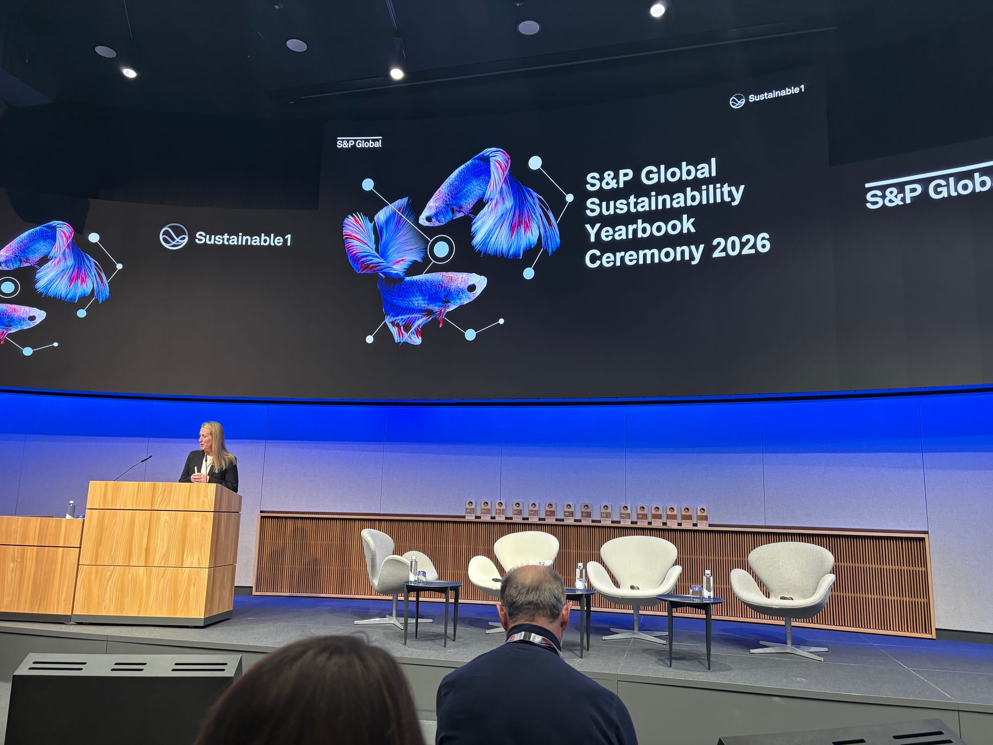 A speaker on stage at the S&P Global Sustainability Yearbook Ceremony 2026 in Zurich, in front of a large screen reading "S&P Global Sustainability Yearbook Ceremony 2026" with the Sustainable1 logo and stylised butterfly graphics